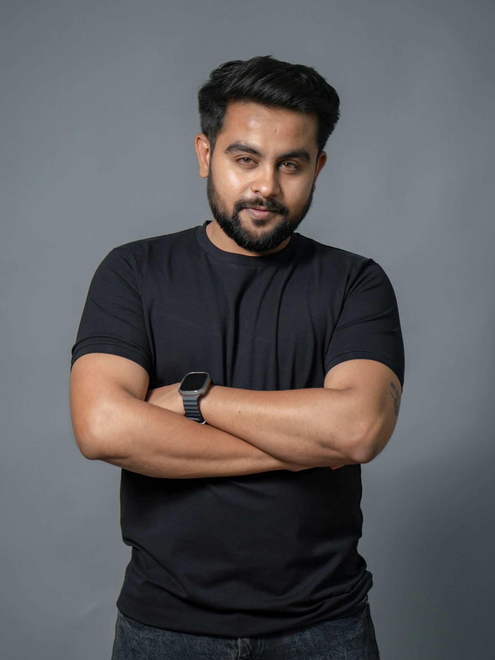 Man wearing a black t-shirt with arms crossed against a gray background